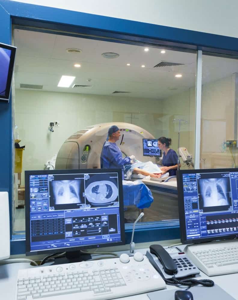 Medical professional doing MRI while one of them is outside the room looking at PACS